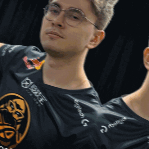 Sports gif. A photograph of two men in glasses wearing black ENCE esports jerseys and standing next to each other with blank stares. One man puts his hand on the other's chest, as if he's holding him back. Caption reads, "Hol up, let him cook." 