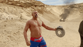 Digital art gif. Chuck Liddel moves out of the way of a wrecking ball and then smashes it with his head, leaving a huge dent in the ball. He then looks at us like nothing happened.