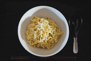Video gif. Bowl of ramen noodles begins to fill up with soup, veggies, meat, and condiments.