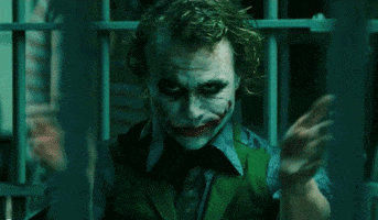 Movie gif. Actor Heath Ledger as the Joker in The Dark Knight menacingly claps from behind prison bars with a threatening gaze.