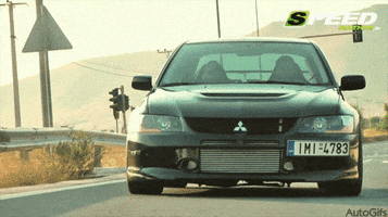 Video gif. Sporty silver Mitsubishi Lancer drives toward us with a European license plate.
