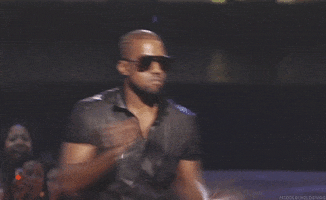 Celebrity gif. Kanye on stage, holding a microphone, frowning and shrugging.