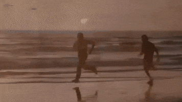 Movie gif. Sylvester Stallone as Rocky and Carl Weathers as Apollo in Rocky. Both of them are booking it down a beach, running as fast as they can. Apollo turns around to run backwards, outpacing Rocky even while backwards. 