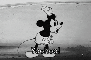 Disney gif. Black and white era Mickey Mouse stands in a field, smiling and waving at someone offscreen as he says, "Yoohoo!"