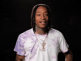 Celebrity gif. Musician Wiz Khalifa smiles, playfully shrugs and raises his hands as if to say "oh well."