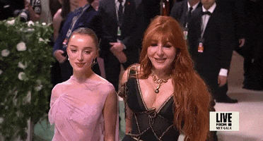 Met Gala 2024 gif. Slomo of Phoebe Dynevor wearing an ethereal Victoria Beckham gown, posing for the cameras holding hands with Charlotte Tilbury, adjust with an elegant tip of her chin.
