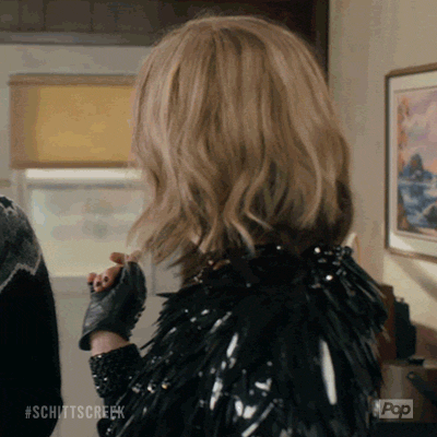 Schitt's Creek gif. Catherine O'Hara as Moira turns to look at someone off screen with a big, open-mouthed smile, quickly scanning her eyes up and down. 
