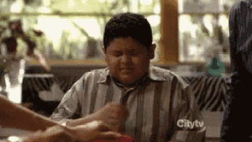 TV gif. Rico Rodriguez as Manny in Modern Family sits at a table during a family meal. Clearly distressed, he squeezes his eyes shut and performs the sign of the cross. 
