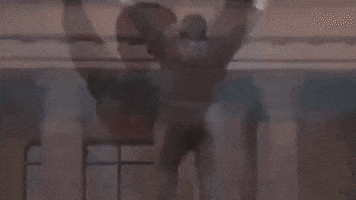 Movie gif. Sylvester Stallone as Rocky Balboa in the movie, "Rocky" raises his fists over his head as he bounces up and down in victory against a smoggy city background.