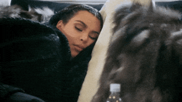 Celebrity gif. Kim Kardashian is bundled up in blankets, sleeping peacefully on a couch.