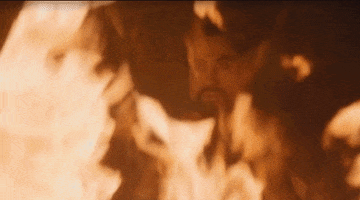 Game of Thrones gif. Emilia Clarke as Daenerys Targaryen pushes a flaming pyre to the ground in front of Joe Naufahu as Khal Moro in a room engulfed in flames.