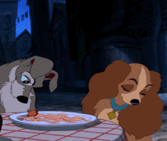 Disney gif. A clip from the iconic spaghetti scene from Lady and the Tramp. Using his nose, Tramp nudges a meatball across a dinner plate towards a flattered Lady.