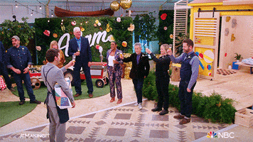 Reality TV gif. A man applauses in congratulations as a group of people on the show Making It, hold up champagne glasses in a toast.