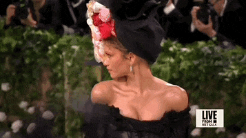 Met Gala 2024 gif. Zendaya, looking over her shoulder, turns back toward us, revealing her big floral hat.