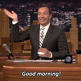 TV gif. Jimmy Fallon behind his talk show desk smiling and waving at the audience.