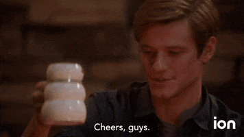 TV gif. Isabel Lucas as Samantha Cage on MacGyver clinks Christmas mugs with Lucas Till as Angus MacGyver as she says, “Cheers.” He responds with, “Cheers, guys.”