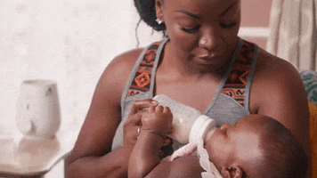 Video gif. Woman cradles and gazes down at her baby while feeding her a bottle and rocking gently side to side.