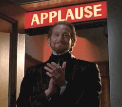 Video gif. A man in an elaborate suit smirks slightly as he slow claps beneath a flashing light box that says, "Applause."