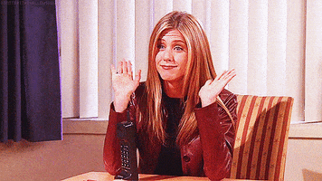 Friends gif. Jennifer Aniston as Rachel Green sits in a red leather jacket with a black block phone resting in front of her. She gives a small wave with both of her hands and smiles fakely while saying, "Hi."