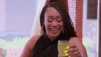 Reality TV gif. Tami Roman of Basketball Wives smiles and sips her iced tea.