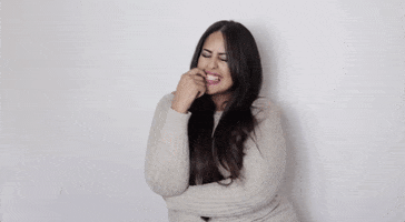Video gif. Brunette woman rests her elbow on her arm crossed over her belly, with her finger on her mouth, then leans forward with a burst of laughter.