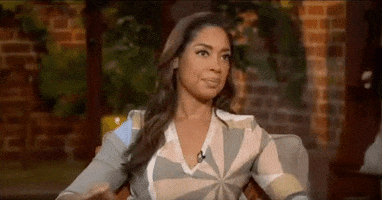 Celebrity gif. Gina Torres folds her hands and places them on her lap before giving a demure closed lipped smile and looking up at the interviewer.