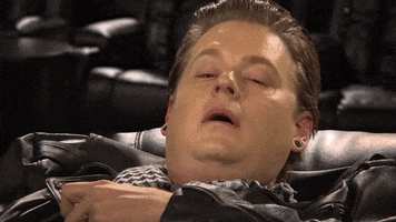 TV gif. Tim Heidecker sits reclined in a chair with droopy red eyes and a confused, open mouth. He drunkenly bops his head around as he picks his head up to look around. 