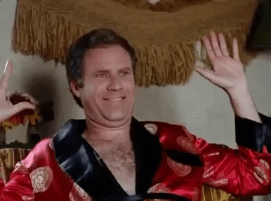 Movie gif. Actor Will Ferrell as Chaz in the Wedding Crashers sits in a red robe. He excitedly punches the air with both hands, and gives a cheeky smile that widens as he celebrates. 