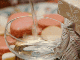 Holiday gif. Champagne pours rapidly into a glass, which is revealed to be just one of an entire ascending stack of filled champagne glasses. The glass on top is overflowing, and we get a close-up of the drink bubbling over and flowing down the sides of the glass.