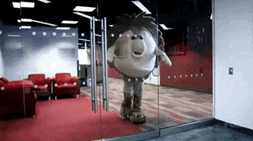 Video gif. Person in a hedgehog mascot costume walks into a glass door in an office space.