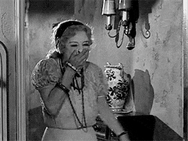Movie gif. Bette Davis, as Jane in What Ever Happened to Baby Jane, covers her mouth while laughing, rushes through a doorway, shuts the door and leans against it, and laughing.