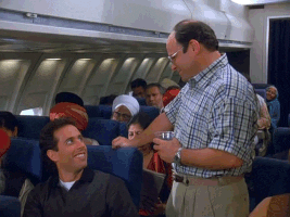 TV gif. Jason Alexander as George on Seinfeld stands in an airplane aisle next to a sitting Jerry. He points to Jerry as he turns sarcastically to the rest of the plane. Text, "Funny guy right here."