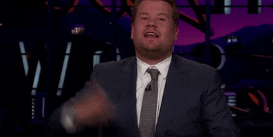 TV gif. James Corden on the Late Late Show looks at us while fanning himself with his hand. He huffs out a big breath of air like it's getting steamy on set. 