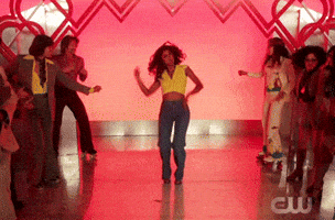 TV gif. Vella Lavell as Heather in Crazy Ex-Girlfriend boogies wildly down an aisle between two lines of people dancing.