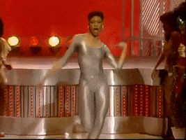 TV gif. A woman on the seventies show Soul Train in a gold bodysuit dances with people lined up around her watching her bust a move. She struts, does a huge kick, thrusting her body around, until she does a full split. 