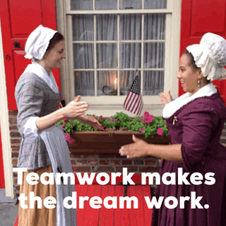Video gif. Two women dressed in colonial-style clothes do a fist bump handshake. Text, "Teamwork makes the dream work."