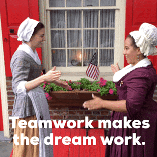 Video gif. Two women dressed in colonial-style clothes do a fist bump handshake. Text, "Teamwork makes the dream work."