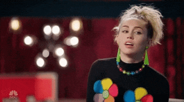 Reality TV gif. Miley Cyrus on the Voice looks around, nodding, with her mouth open a bit as if saying, “uh huh.”