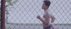 Music video gif. From a song by M City Jr, through a chain-link fence, we see two women running.