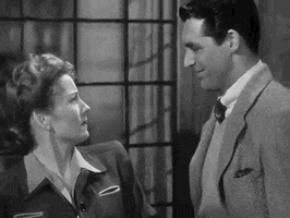 Movie gif. Joan Fontaine as Lina and Cary Grant as Johnnie in Suspicion. Lina looks at Johnnie chuckling at her and she stares at him before reaching up to grab his neck to bring him down for a deep kiss.