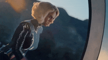 Music video gif. From video for Chained to the Rhythm, Katy Perry, dressed in a shiny superhero-esque costume and a blonde curly bob, appears to be running on a hamster wheel.