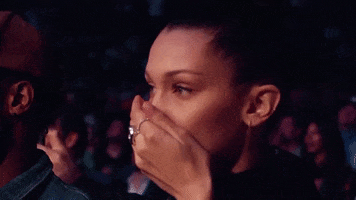 Celebrity gif. Bella Hadid sits in the audience at a UFC game. She covers her mouth and her eyes are wide with shock.