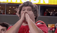 TV gif. A nervous man watching an NCAA college football game bounces up and down and folds his hands in prayer.