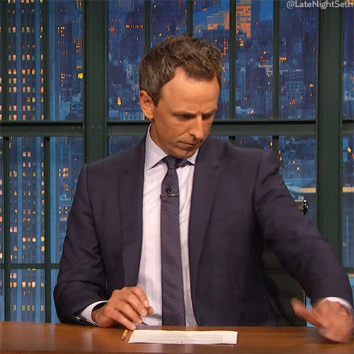 Late Night gif. Holding an imaginary phone, Seth Meyers scrolls and then stops, looking annoyed and rolling his eyes dramatically.