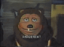 Video gif. Lion animatronic from ShowBiz Pizza slightly tilts its head with its blue eyes widening and tongue sticking out. Text reads in a pixelated, arcade-like font, "Amazement."
