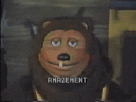 Video gif. Lion animatronic from ShowBiz Pizza slightly tilts its head with its blue eyes widening and tongue sticking out. Text reads in a pixelated, arcade-like font, "Amazement."