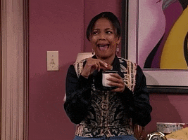 TV gif. Kim Fields as Regine holds a cookie over a mug as she looks to the side and laughs. 