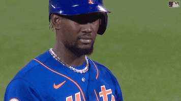 Sports gif. Ronny Mauricio on the New York Mets on the field wearing a batter's helmet. He kisses his hand and then sends it away with a calm, confident expression.