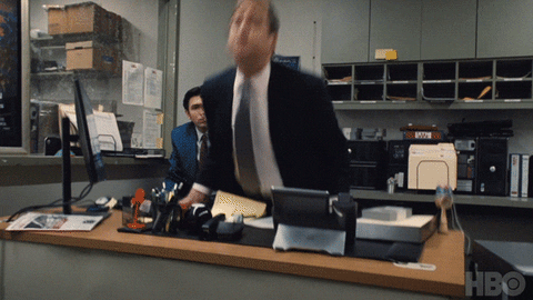TV gif. Matthew MacFadyen as Tom from Succession flips over a large desk, screaming, spilling its contents everywhere.