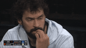 Sports gif. Sergio Llull, captain of Real Madrid of the Spanish Liga ACB and the EuroLeague, is sitting on the sidelines looking extremely anxious as he bites his nails and stares at the court.